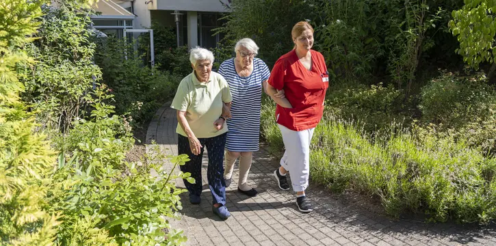 Pflegefachkraft mit zwei Seniorinnen beim Spaziergang
