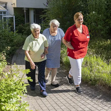 Pflegefachkraft mit zwei Seniorinnen beim Spaziergang