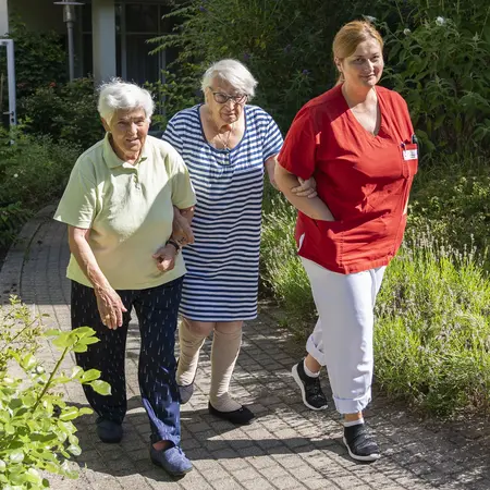 Pflegefachkraft mit zwei Seniorinnen beim Spaziergang